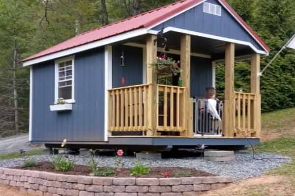 Red white and blue mini shed with porch, pet gate, and window boxes on the exterior